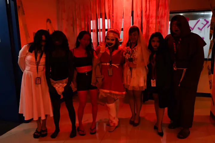 Seven teammates in coordinated horror costumes posing under red lights