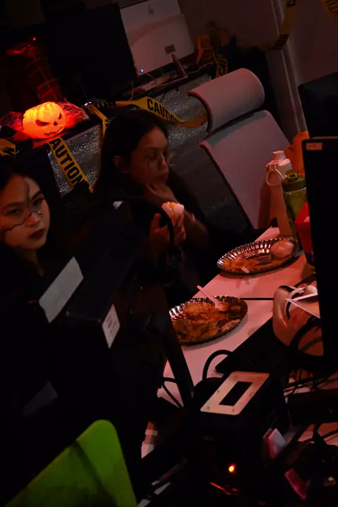 Potluck plates at a desk next to a glowing jack-o'-lantern and caution tape