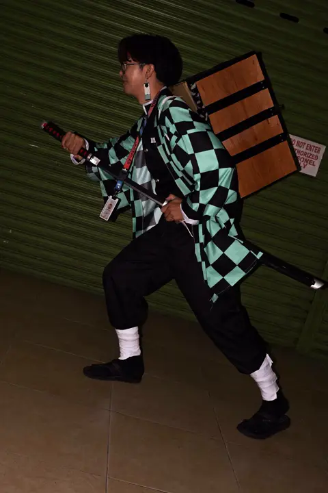 Demon Slayer cosplayer mid-pose with a wooden box on his back