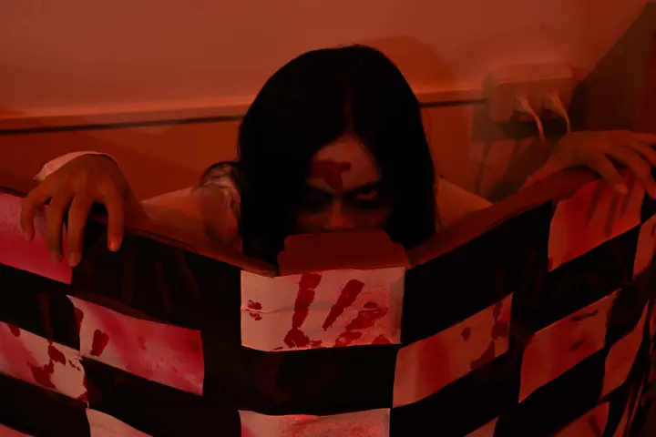 Figure with a bloody face peeking over a striped barrier