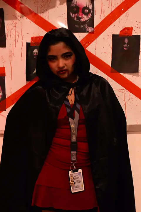 Teammate in a black cloak and red dress against a red-tape wall